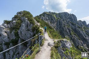 An einer luftigen Stelle sichert ein Geländer die Wanderer