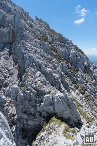 Drehen wir uns nach Süden lässt sich die Linie durch die Westflanke gut einsehen. Zu unseren Füßen bricht der Grat fast senkrecht ab, unten ist am Felsansatz ein großer Steinhaufen zu erkennen. Zu diesem muss abgeklettert werden (II).